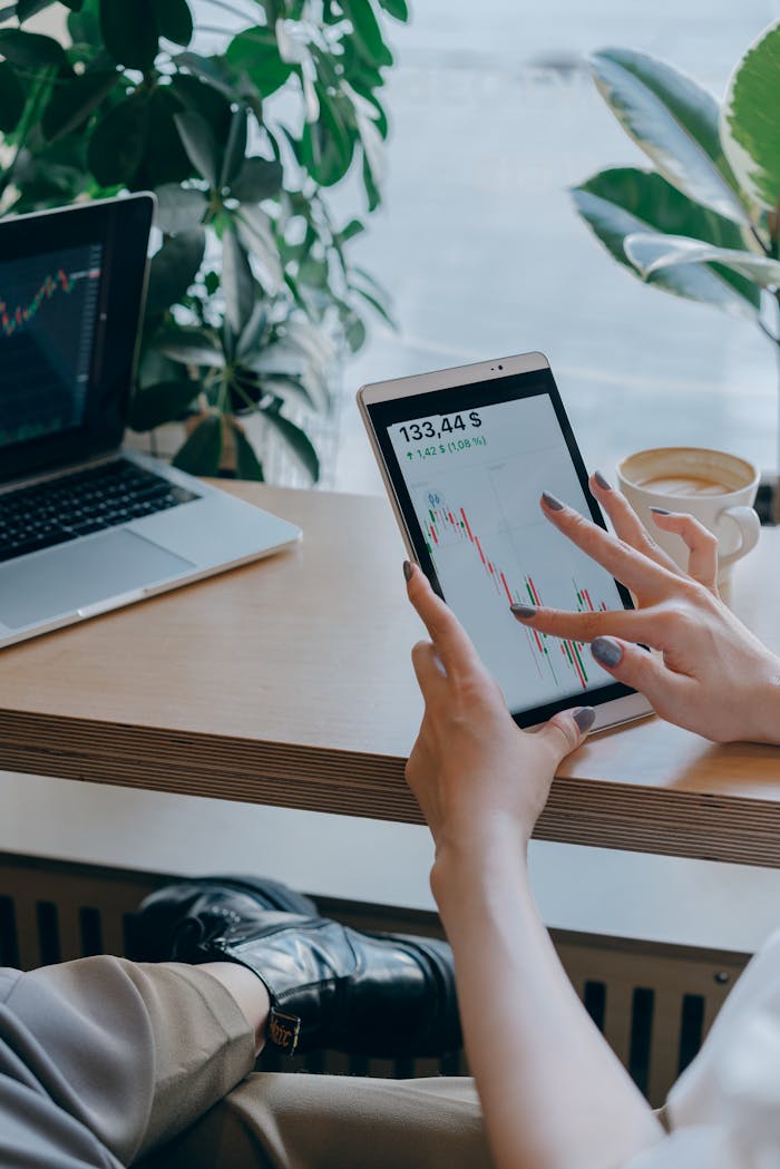 Close-up of hands using a tablet for stock market analysis in a modern office setting.